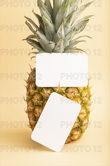 White paper business card with ripe pineapple on orange pastel background. Side view, copy space.
