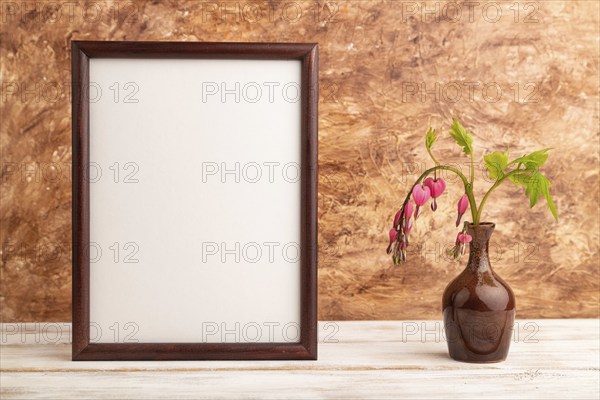 Wooden frame with pink dicentra, broken heart in ceramic vase on brown concrete background. side