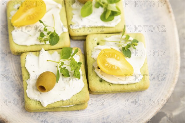 Green cracker sandwiches with cream cheese and cherry tomatoes on gray concrete background. top