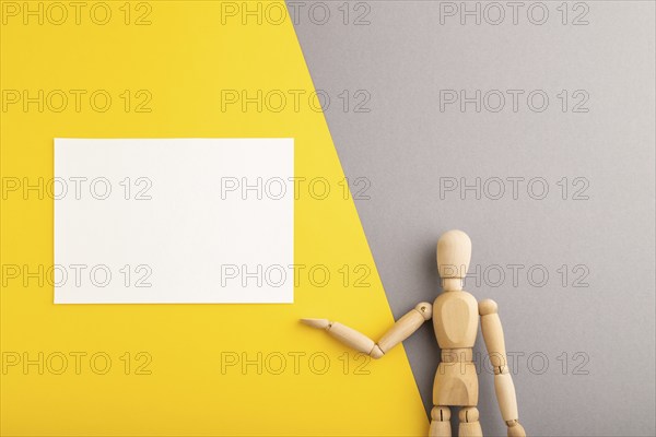 Wooden mannequin holding white blank poster on gray and yellow pastel background. copy space,