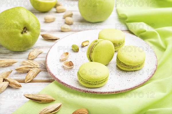 Green macarons or macaroons cakes with cup of coffee on a white wooden background and green linen
