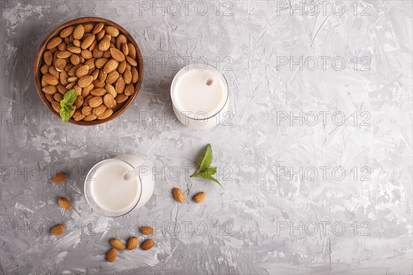 Organic non dairy almond milk in glass and wooden plate with almond nuts on a gray concrete