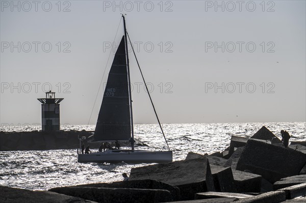 Sailing boat leaving the harbour of Scheveningen, lighthouse at the harbour entrance, Netherlands