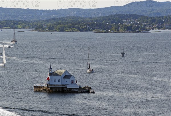 Small lighthouse on an island in the water, surrounded by boats and hills in the distance, Dyna