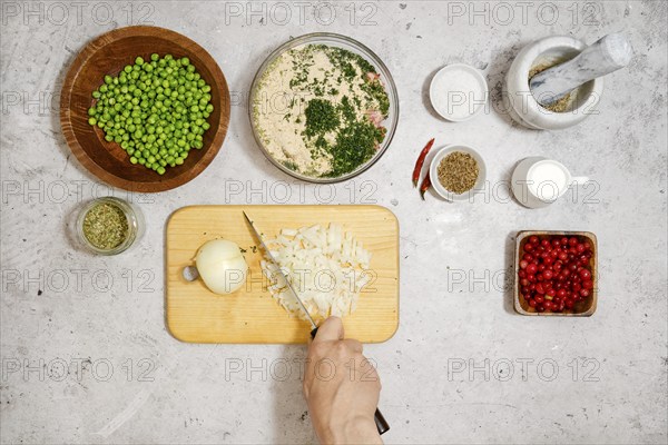 Unrecognizable man cutting fresh onion on wooden chopping board, top view