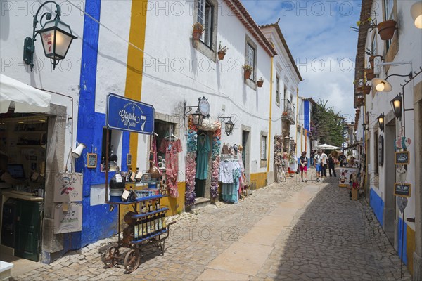 Narrow alley with souvenir shops and colourful clothes, blue and white facades and flowers, R.