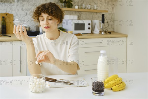 Woman takes out a piece of sugar from a sugar bowl while sitting at kitchen table
