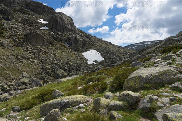 Mountainous landscape with rocky terrain and scattered patches of snow under a blue sky with
