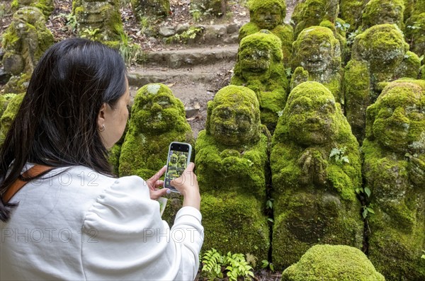 Visitor takes pictures of rakan statues at Otagi Nenbutsu-ji temple, Kyoto, Japan, Asia