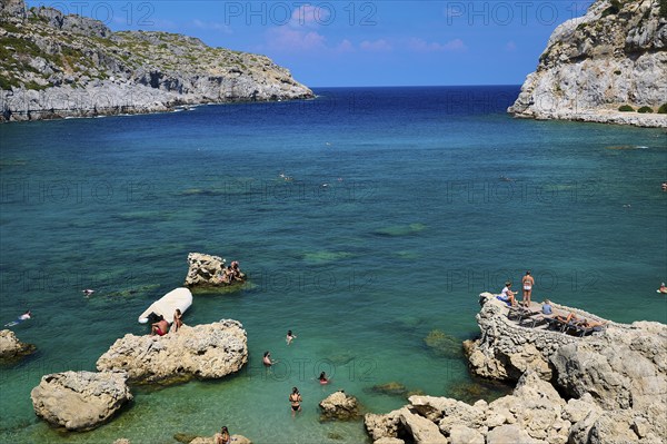 Sunbathing people on rocks on a coast with deep blue water and sunny sky, Anthony Quinn Bay, Vagies