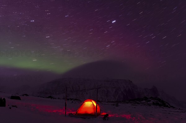 Northern Lights (Aurora borealis) and star trails above an illuminated tent in the valley Stuor