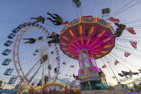 A funfair at dusk with illuminated chain carousel and Ferris wheel, Europa Rad, rides, wave flight,