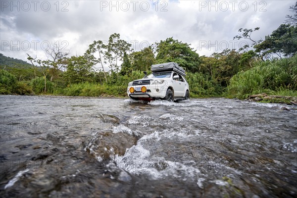 Toyota off-road vehicle with roof tent drives through a wide river in the rainforest, Alajuela