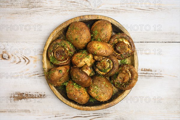A rustic wooden plate with baked champignon mushrooms, each filled with herbs, sitting atop a light