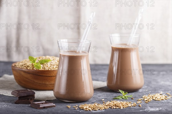 Organic non dairy oats chocolate milk in glass and wooden plate with oats seeds on a black concrete