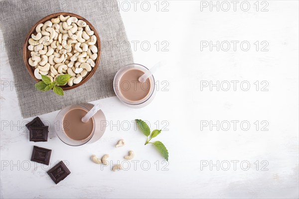 Organic non dairy cashew chocolate milk in glass and wooden plate with cashew nuts on a gray