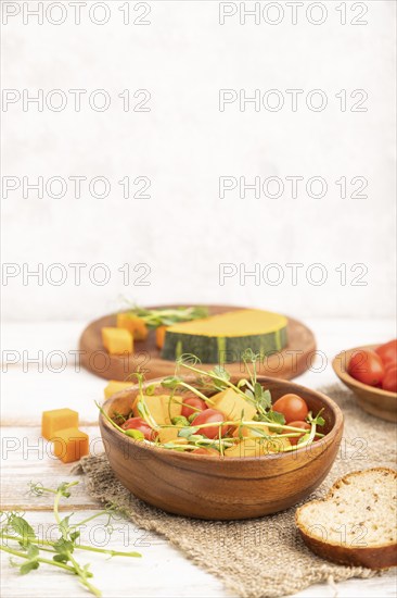 Vegetarian vegetable salad of tomatoes, pumpkin, microgreen pea sprouts on white wooden background