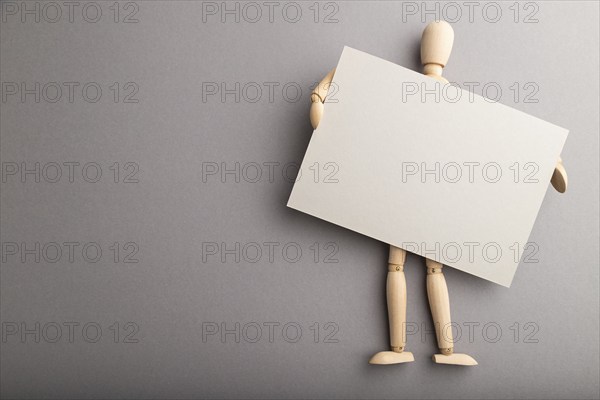 Wooden mannequin holding gray blank poster on gray pastel background. copy space, isolated,
