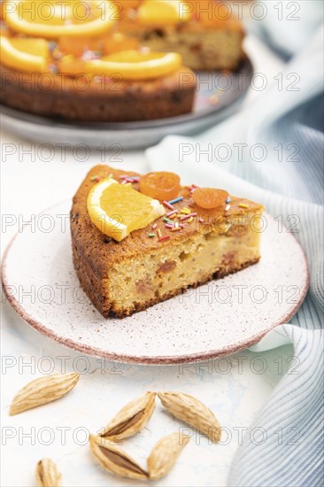 Orange cake with almonds and a cup of coffee on a white concrete background and blue linen textile.