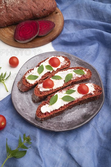 Red beet bread sandwiches with cream cheese and tomatoes on white concrete background and blue