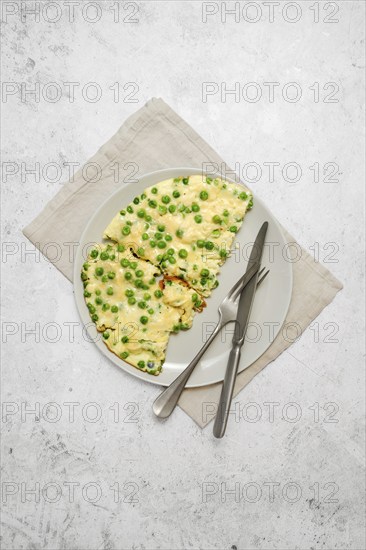 Omelet with fresh green peas and cheese on a plate on a grey stone tabletop