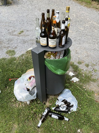 Overflowing rubbish bin, with lots of rubbish, glass bottles next to it, party rubbish, at a