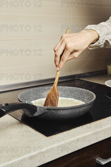 Unrecognizable woman miking scrambled eggs in a frying pan in her kitchen