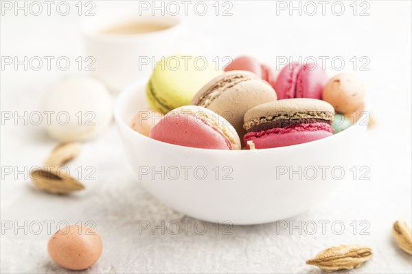 Multicolored macaroons and chocolate eggs in ceramic bowl, cup of coffee on gray concrete