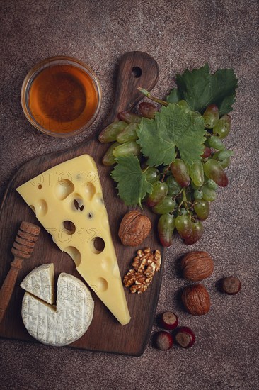 Cheese with big holes, emmental, maasdam, brie cheese, on a cutting board, with grapes and honey,