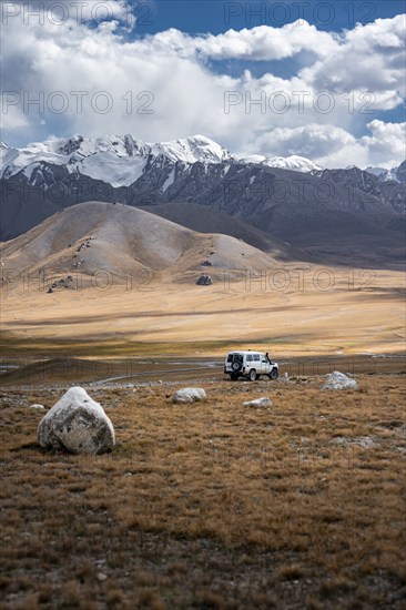 Off-road vehicle on a gravel track, glaciated and snow-covered peaks, Ak Shyrak Mountains, near