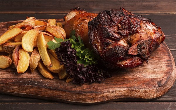 Pork knuckle, in soy-honey sauce, with fried potatoes, on a wooden chopping board, homemade, no