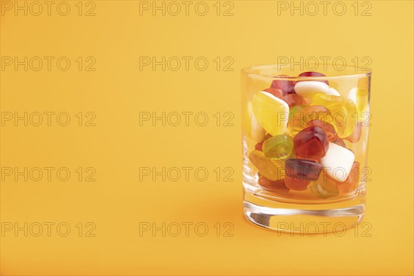 Various fruit jelly candies in drinking glass on orange pastel background. side view, copy space