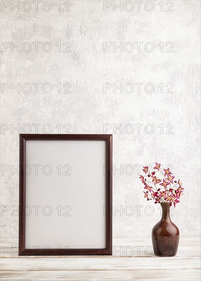 Wooden frame with purple barrenwort flowers in ceramic vase on gray concrete background. side view,