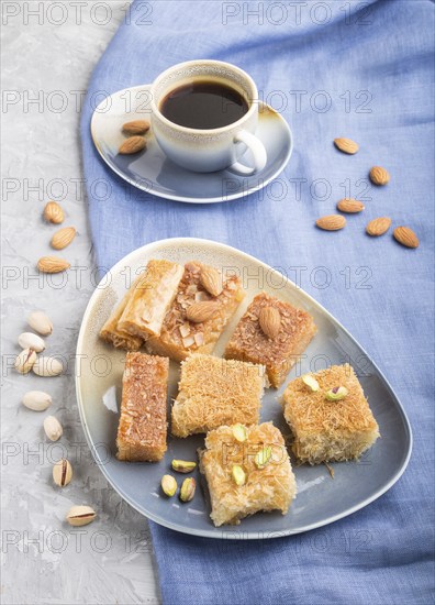 Traditional arabic sweets (basbus, kunafa, baklava) and a cup of coffee on a gray concrete