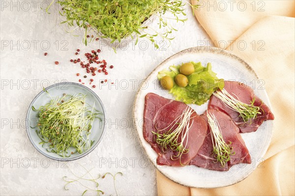 Slices of smoked salted meat with cilantro microgreen on gray concrete background and orange