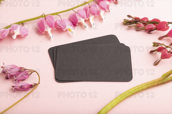 Black business card with pink dicentra, broken heart flowers on pink pastel background. side view,