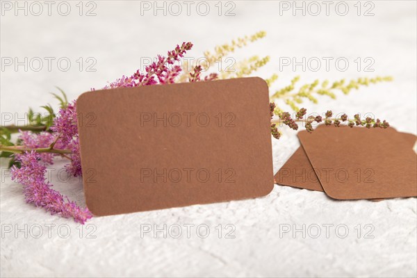 Brown paper business card mockup with purple astilbe flowers on gray concrete background. Blank,