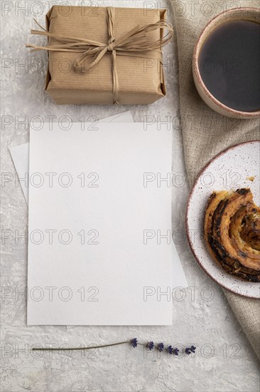 White paper invitation card, mockup with lavender, bun, cup of coffee, linen textile, box on gray
