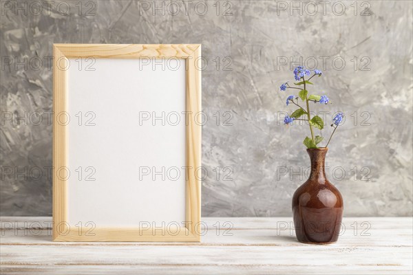 Wooden frame with blue forget-me-not flowers in ceramic vase on gray concrete background. side