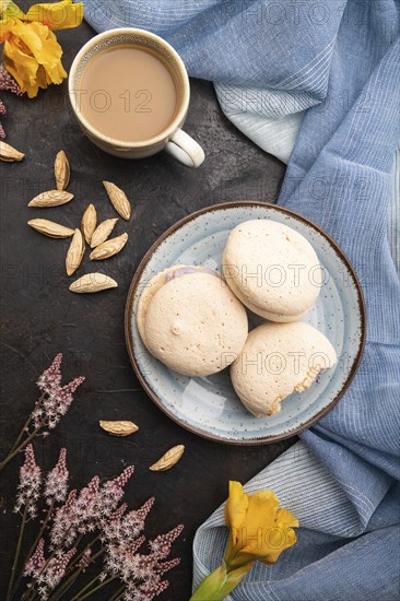 Meringues cakes with cup of coffee on a black concrete background and blue linen textile. Top view,