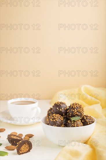 Chocolate caramel ball candies with almonds and a cup of coffee on a white and orange background