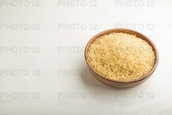 Wooden bowl with raw golden rice. Side view, close up, copy space