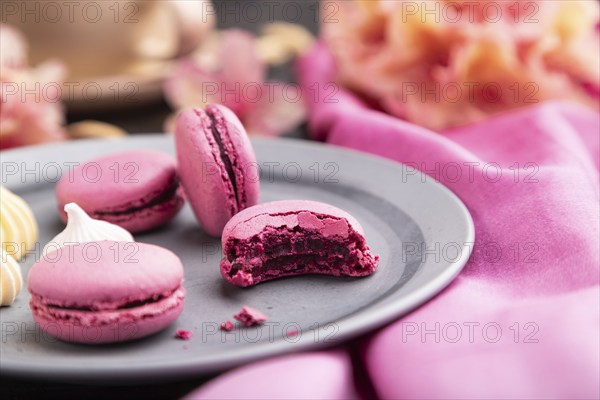 Purple macarons or macaroons cakes with cup of coffee on a black concrete background and pink