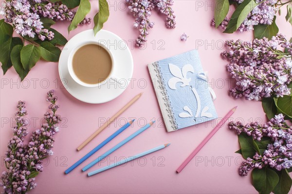 Purple lilac flowers and a cup of coffee with notebook and colored pencils on pastel pink