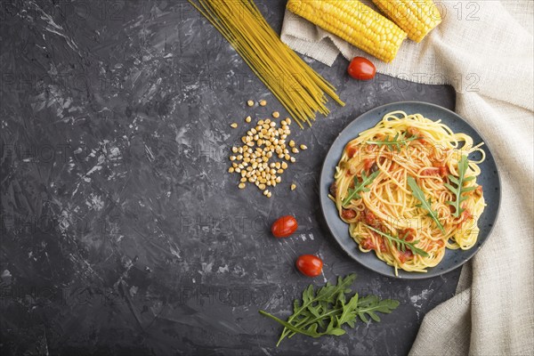 Corn noodles with tomato sauce and arugula on a black concrete background and linen textile. Top