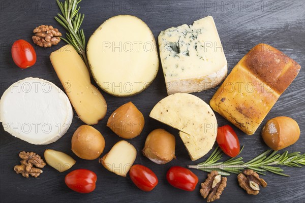 Set of different types of cheese with rosemary and tomatoes on a black wooden background. Top view,