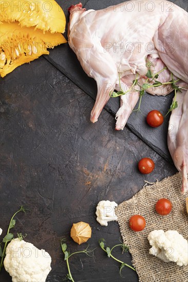 Whole raw rabbit with pumpkin, tomatoes, pea sprouts on a black concrete background and linen