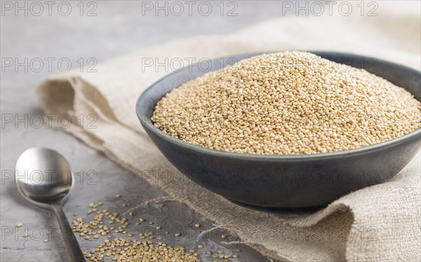 Blue ceramic bowl with raw white quinoa seeds on a gray concrete background and linen textile. Side