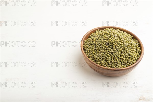 Wooden bowl with raw green mung bean on a white wooden background. Side view, close up, copy space