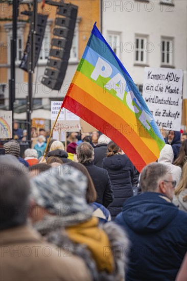 People at a public gathering with a big peace flag 'Pace' and speakers on a stage, Against Right